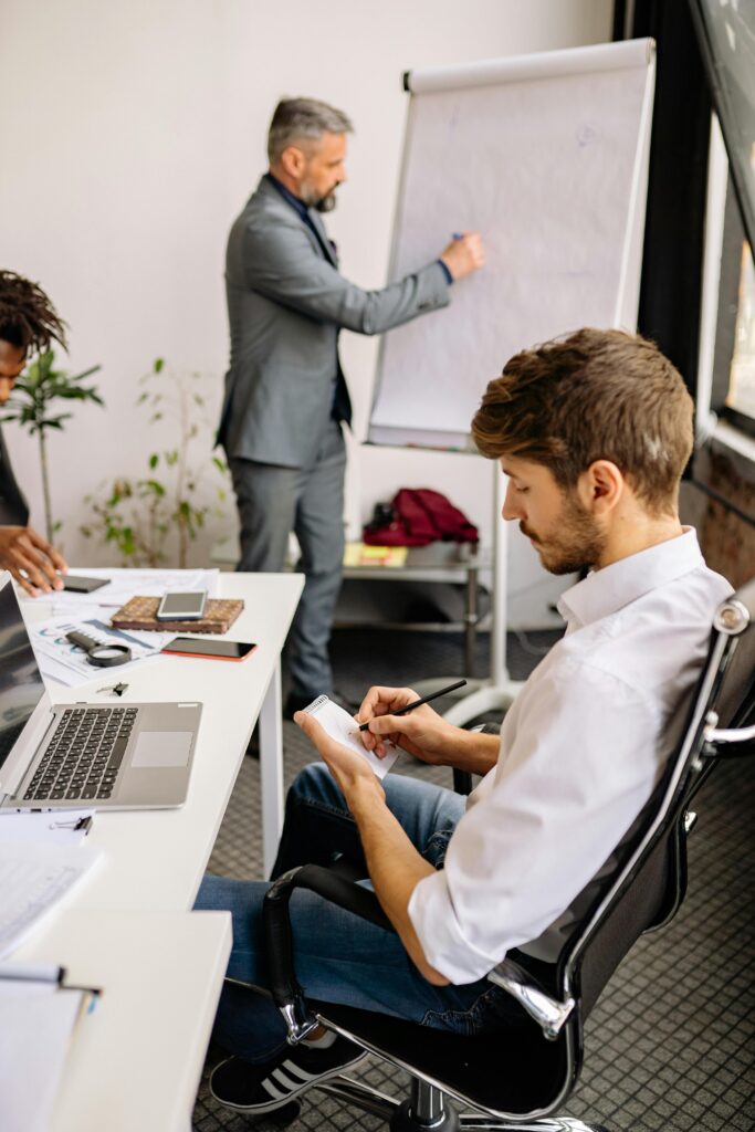 Business professionals engaged in a collaborative meeting, taking notes and discussing ideas on a flipchart.